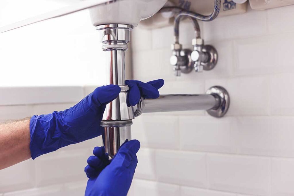 A close-up of a chrome bathroom faucet with a visible water droplet at the spout.