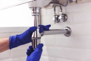 A close-up of a chrome bathroom faucet with a visible water droplet at the spout.