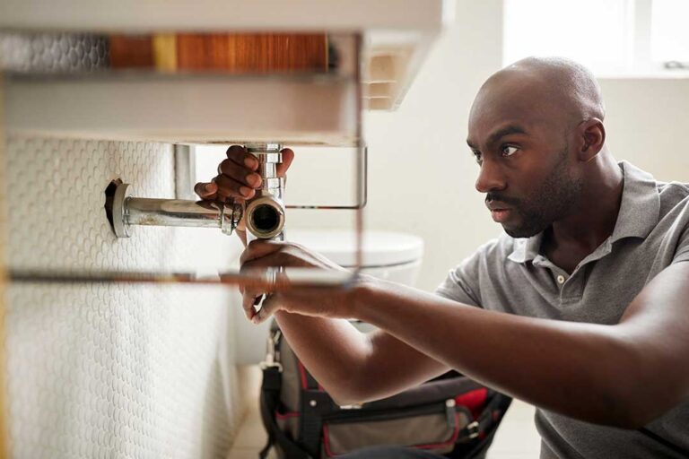 A person in work clothes examining a leaking toilet with a towel and toolbox nearby.