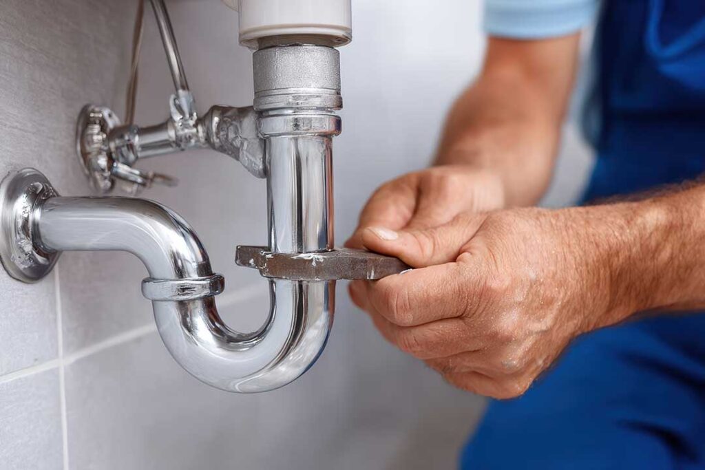 Person testing lukewarm shower water beside a residential water heater and bathroom fixtures