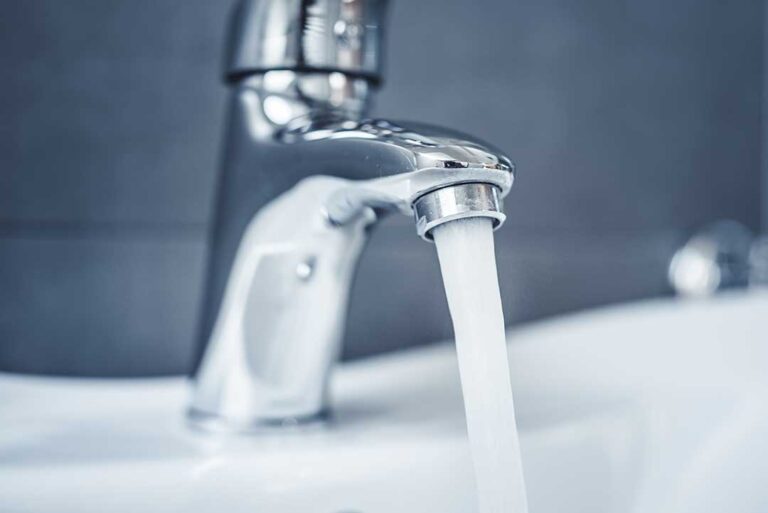 Person wiping a chrome faucet and porcelain sink with a soft microfiber cloth in a clean bathroom.